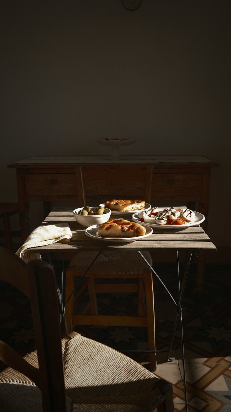 Platos de focaccia, aceitunas y ensalada Caprese sobre una mesa rústica.