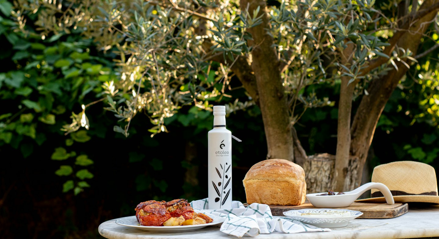 Botella de aceite de oliva Etolea con pan y tomates rellenos al aire libre.